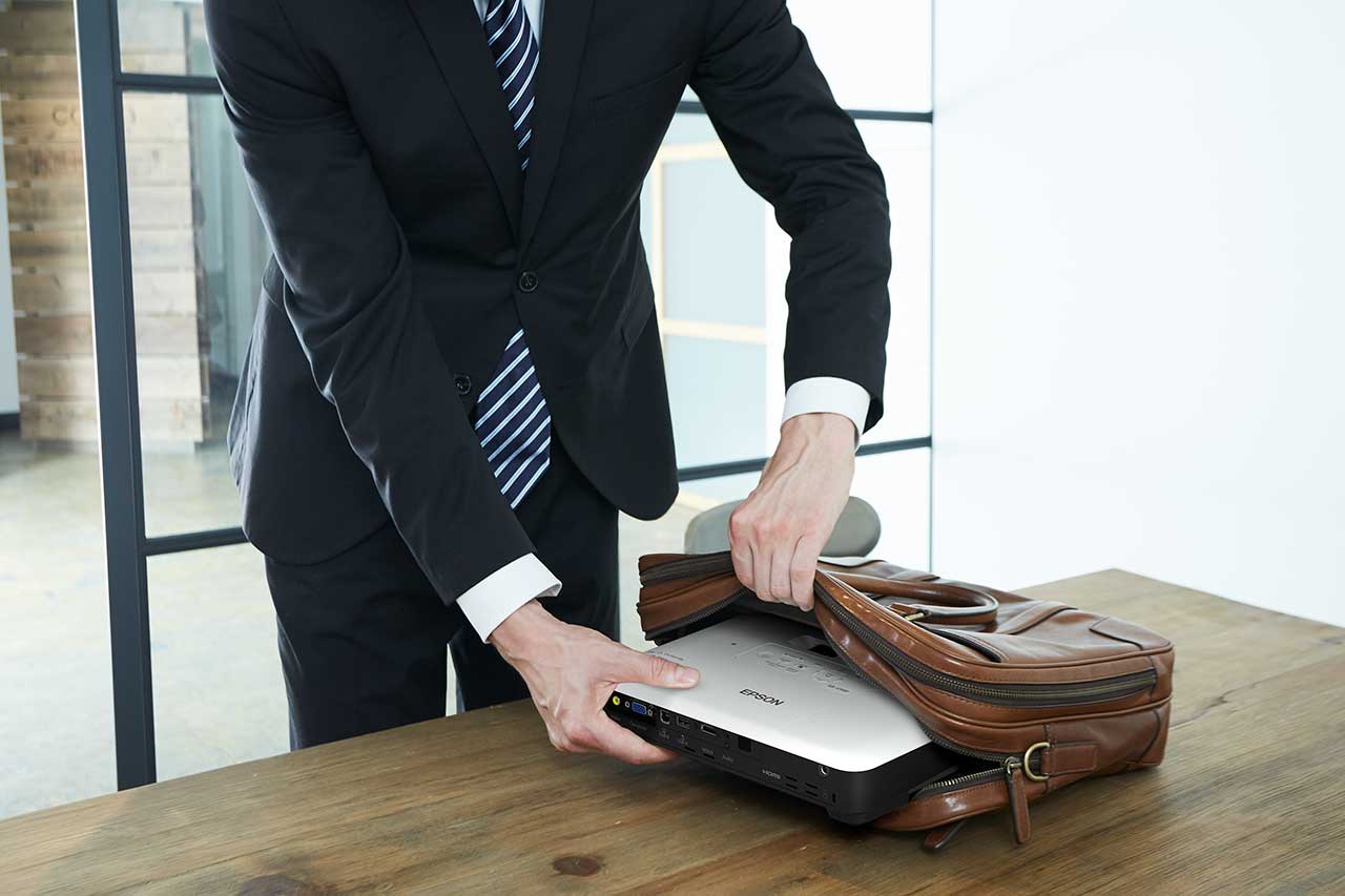 person in a suit slipping the Epson EB 1780W portable projector out of a laptop case