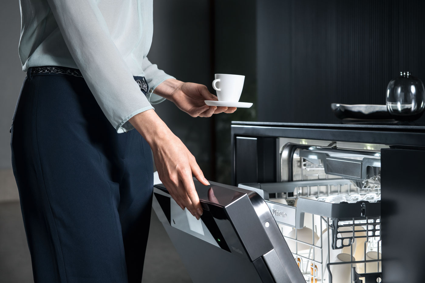 Woman putting a tea cup into an open Miele dishwasher